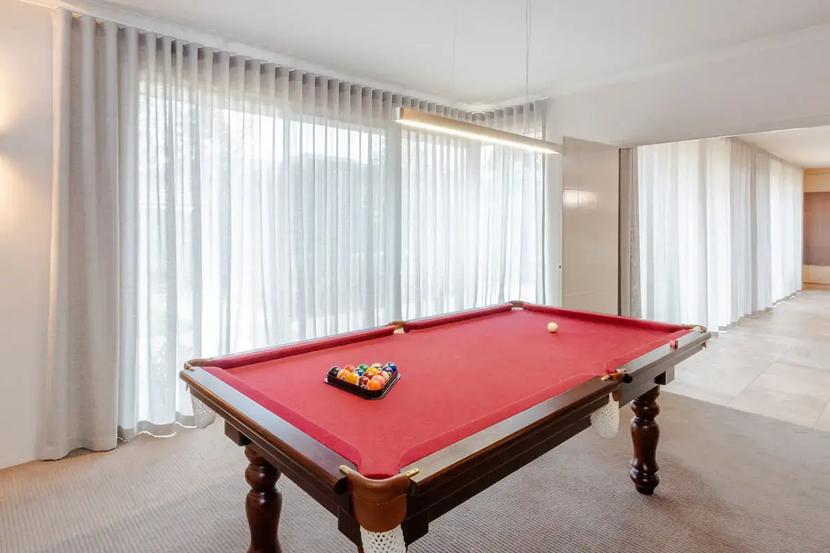 Full-height sheer curtains across wide windows in a finished entertainment room.